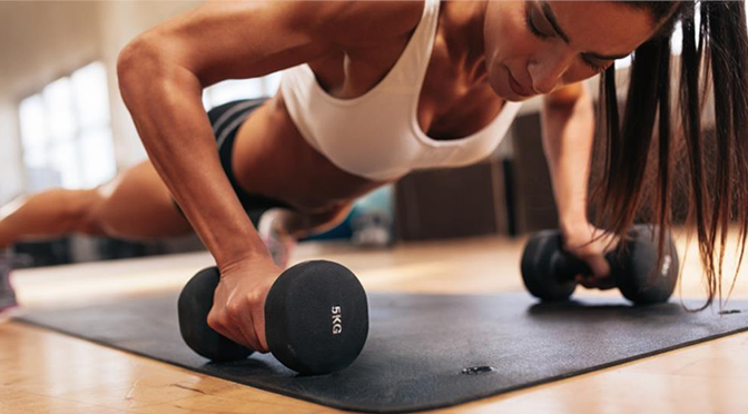 Woman with ponytail doing plank with black rubber dumbbells on black mat
