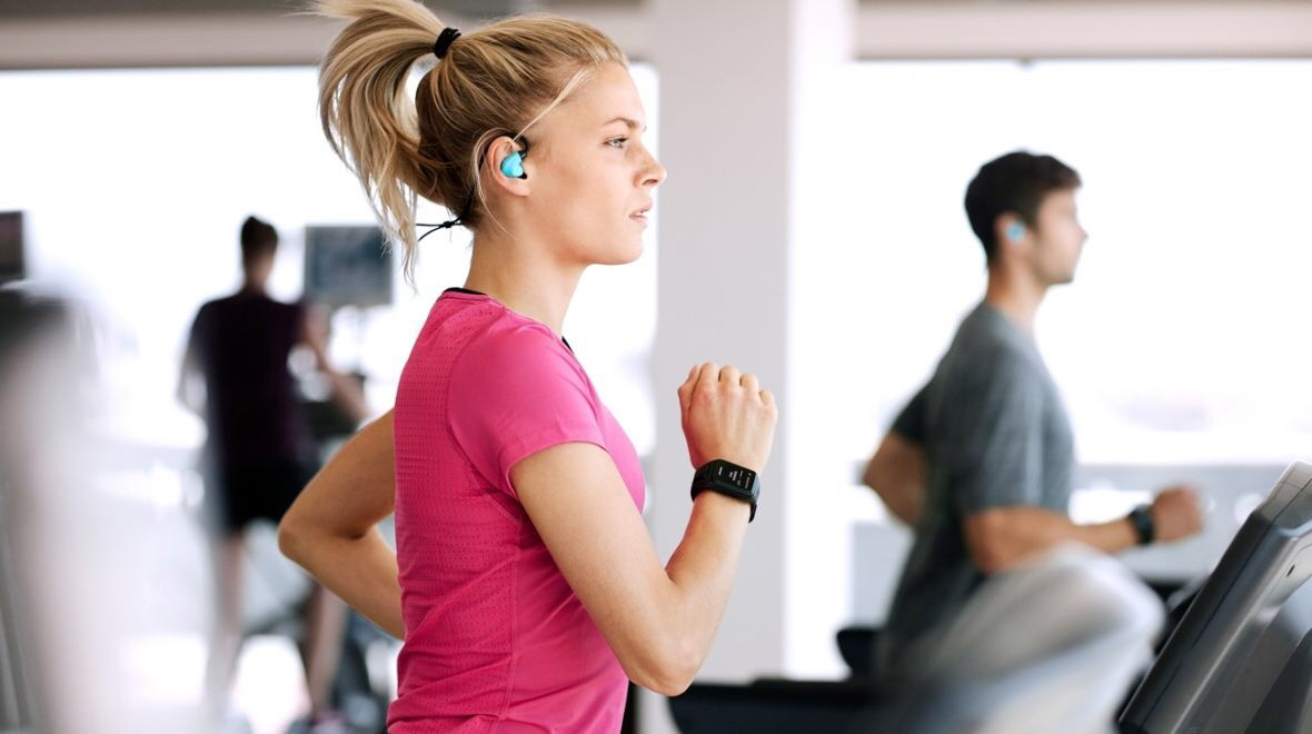 Blonde woman running on treadmill in pink shirt with over the ear headphones and fitness watch