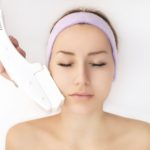 Woman with pink spa headband receiving laser skincare treatment types