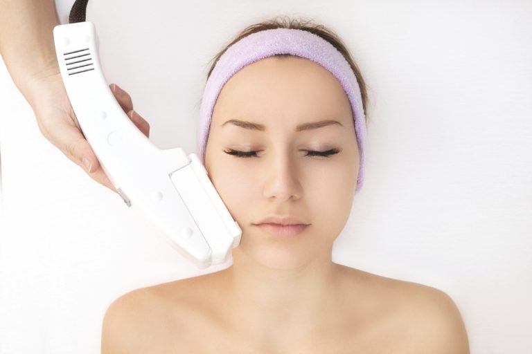 Woman with pink spa headband receiving laser skincare treatment types