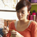 Young Woman Sitting In Chair Knitting Cropped Redhead Hair