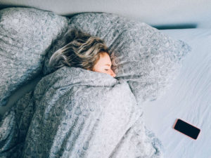 Sleep blonde woman wrapped up in bed blanket comforter phone