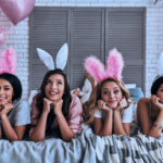 Four attractive young women in bunny ears smiling while lying on the bed