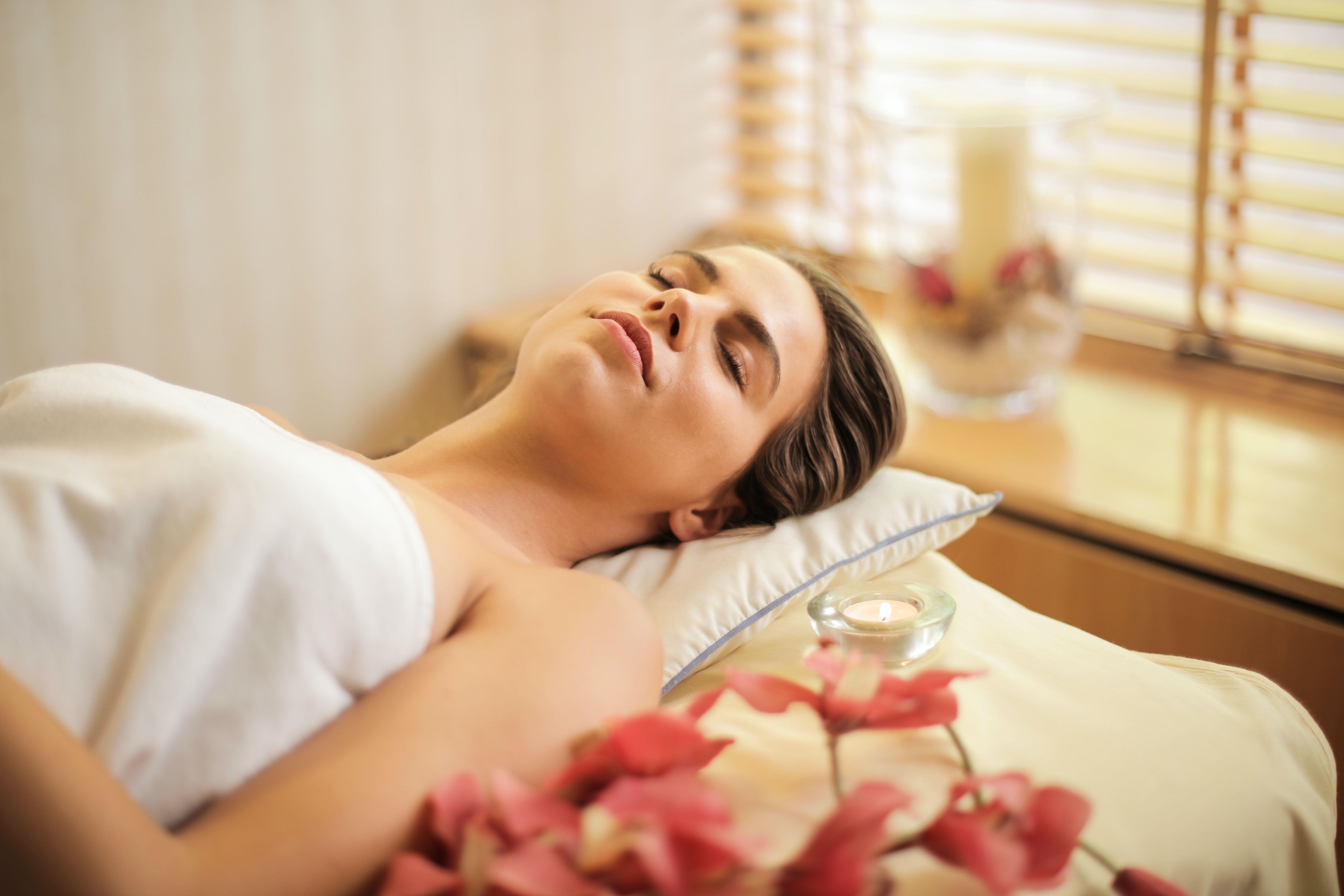 woman-in-wrapped-in-white-towel-lying-on-bed-with-eyes-closed spa