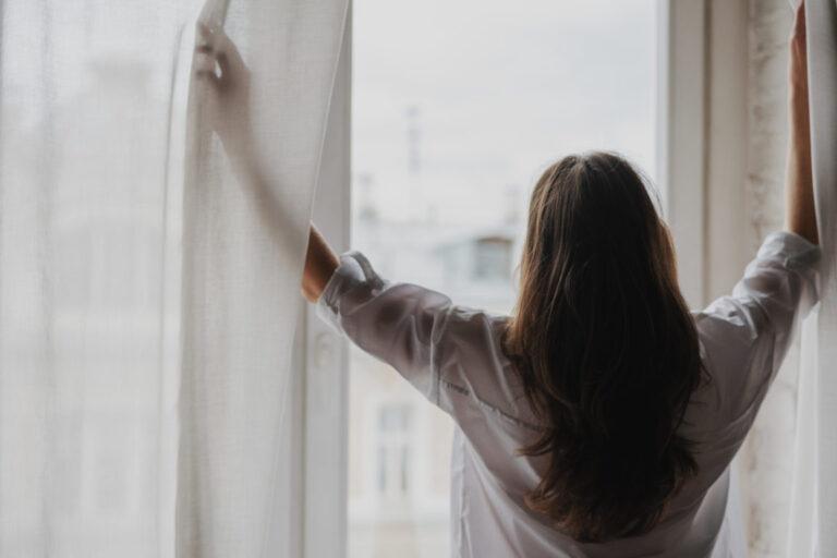 Young brunette woman with long hair opening the curtains